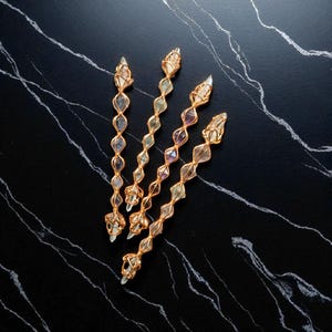 May include: Four vertical wands featuring clear and multi-colored crystals encased in gold-toned wire wrapping. Each wand consists of a series of small, pointed crystal segments linked together in a linear, repeating diamond-shaped pattern.
