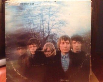 May include: A vintage record album cover featuring a group of five people. The album cover is a light blue color with a faded, blurry image of the people. The people are all wearing dark clothing and have long hair. The album cover has the text "Stereo" printed on it.