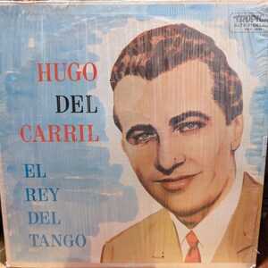 May include: Vintage vinyl record album cover featuring a portrait of Hugo Del Carril. The album cover has a blue and white background with red and white text that reads "Hugo Del Carril El Rey Del Tango".