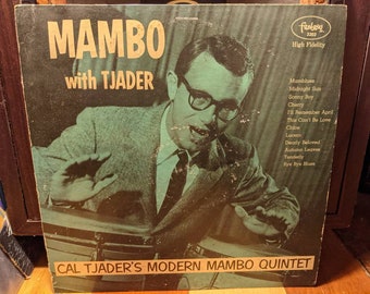 Può includere: Copertina di un album in vinile vintage per "Mambo with Tjader" di Cal Tjader's Modern Mambo Quintet. La copertina presenta un'immagine in bianco e nero di un uomo con occhiali e un abito. Il titolo dell'album e il nome dell'artista sono in testo bianco.