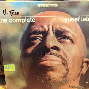 Puede incluir: Portada del álbum "The Complete Yusef Lateef" con un primer plano del rostro de Yusef Lateef. La portada del álbum tiene el logotipo de Atlantic Records. El título del álbum y el nombre del artista están en texto blanco. El nombre del artista está en una fuente sans-serif.
