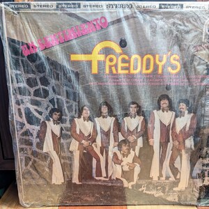 May include: A vintage vinyl record album cover featuring a group of men in white and brown suits. The album is titled "El Sentimiento" by "Freddy's".