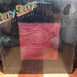 Puede incluir: Un álbum de vinilo titulado "Fancy Sledge - I'll Be Your Everything". La portada del álbum tiene un fondo negro con el nombre del artista en fuente azul y dorada. Un cuadrado de arte abstracto rojo y rosa está en el centro.