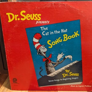 May include: A vintage Dr. Seuss album cover. The cover is red with the title "Dr. Seuss presents The Cat in the Hat Song Book" in yellow and blue. The Cat in the Hat character is illustrated playing a piano. The album is a Camden release.