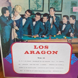 May include: Vintage vinyl record album cover for "Los Aragon Vol. 13." The cover features a group of men in suits and bow ties, with a woman, around a pool table. The album title is in red and white text.