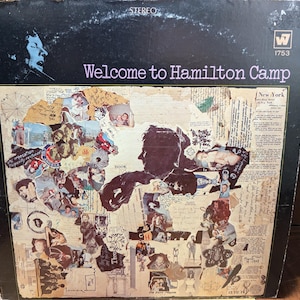 Può includere: Una copertina di un album di vinile vintage con un collage di immagini e testo. L'album è intitolato "Welcome to Hamilton Camp" e presenta una foto in bianco e nero del viso di un uomo nell'angolo in alto a sinistra. La copertina dell'album è in una cornice marrone.