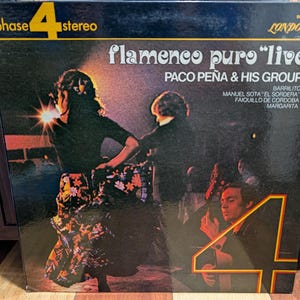 Peut inclure: Pochette de disque vinyle vintage pour "Flamenco Puro 'Live'" de Paco Peña & His Group. La couverture présente une image sombre de danseurs et musiciens de flamenco. Le titre de l'album et l'artiste sont bien en évidence.