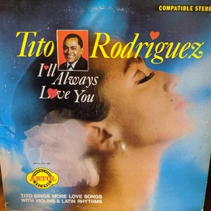 Puede incluir: Portada de álbum de vinilo vintage de Tito Rodríguez, con un retrato del artista y el perfil de una mujer. El título del álbum es "I'll Always Love You". La portada tiene un fondo azul y blanco con el texto "Compatible Stereo".