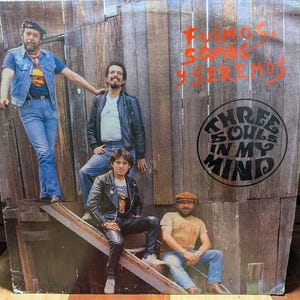 May include: Vintage album cover featuring the band Three Souls in My Mind. The cover shows four men posing on wooden steps. The album title is in a circular design, with the words "Three Souls In My Mind". The background is a wooden wall with text in Spanish.