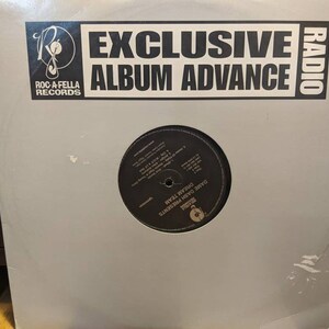 May include: A vinyl record in a white sleeve with the text "EXCLUSIVE ALBUM ADVANCE" and "RADIO." The record label is "ROC-A-FELLA RECORDS." The record itself is black with white text, and the artist is "DAME DASH PRESENTS DREAM TEAM."