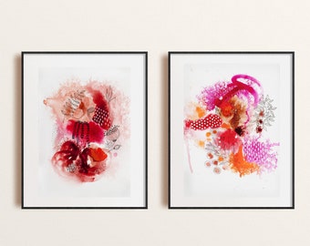 May include: Two framed abstract watercolor paintings with pink, red, and orange colors. The paintings are on a white background and are framed in black.