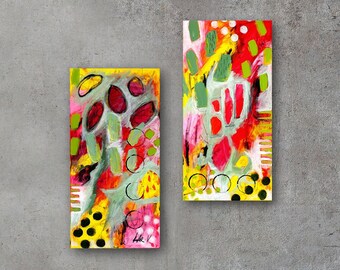 Op de afbeelding: Twee abstracte schilderijen met een kleurrijk, geometrisch ontwerp. De schilderijen zijn ingelijst en hangen aan een grijze muur. De schilderijen zijn in moderne stijl en bevatten felle kleuren zoals rood, geel, groen en zwart.