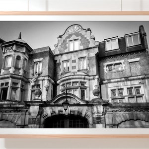 May include: Black and white photograph of a large, ornate building with a grand entrance. The building has a symmetrical facade with multiple windows and a decorative archway. The building appears to be made of brick and stone.