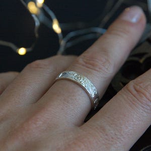 Pu&ograve; includere: Un anello a fascia d'argento con un design floreale testurizzato.