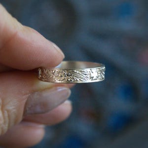 Pu&ograve; includere: Un anello a fascia d'argento con un design floreale dettagliato e un motivo a stella.