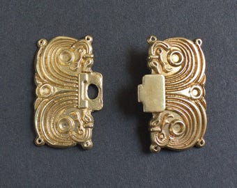 Puede incluir: Dos cierres dorados ornamentados, cada uno con un diseño intrincado y arremolinado. Un cierre tiene un pestillo rectangular, el otro un orificio correspondiente. Los cierres son probablemente para joyería o fines decorativos.