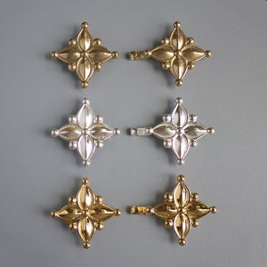 Puede incluir: Seis abalorios decorativos de metal en forma de estrella con un diseño en relieve. Tres abalorios son dorados y tres son plateados.