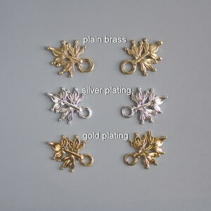 Pu&ograve; includere: Primo piano di ciondoli decorativi a forma di foglia in metallo in ottone naturale, placcatura argento e placcatura oro. Ogni ciondolo presenta un design dettagliato a forma di foglia con un piccolo anello per il fissaggio. Il testo "plain brass", "silver plating" e "gold plating" &egrave; visibile.