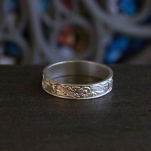 Pu&ograve; includere: Un anello a fascia d'argento con un intricato design floreale.