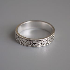 Pu&ograve; includere: Un anello a fascia d'argento con un design intricato di fiori e croci.