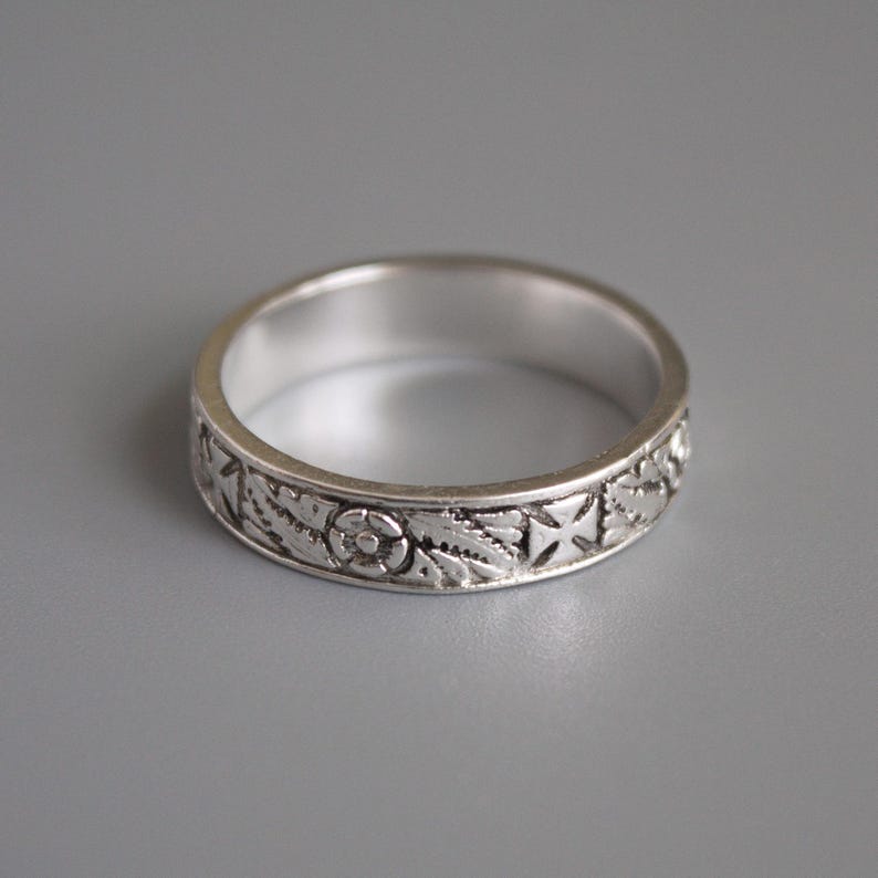 Pu&ograve; includere: Un anello a fascia d'argento con un design intricato di fiori e croci.