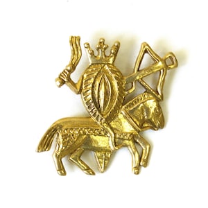 Peut inclure: Broche en métal doré représentant un chevalier à cheval. Le chevalier tient une épée et un bouclier, et porte une couronne. Le cheval est également orné. La broche est sur fond blanc.