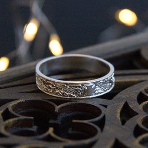 Pu&ograve; includere: Un anello d'argento con un intricato design floreale inciso attorno alla fascia.