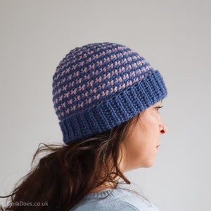 May include: A blue and pink crocheted beanie hat with a textured pattern. The hat is worn by a person with long brown hair.