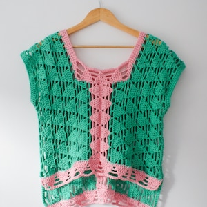 Puede incluir: Un top de ganchillo de color verde y rosa. El top tiene un escote amplio y abierto y mangas cortas. El top está hecho con un delicado patrón de punto abierto.