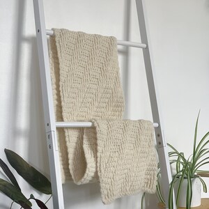May include: A white wooden ladder with two white knitted blankets draped over the rungs.