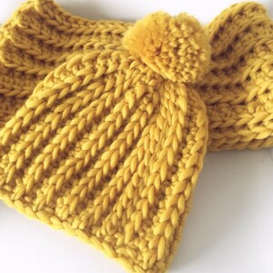 May include: A yellow knitted hat with a pom-pom on top. The hat is made of a thick yarn and has a ribbed texture.
