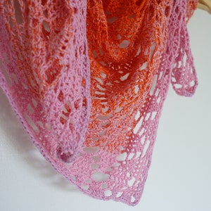 May include: A crocheted shawl with a pink and orange ombre design. The shawl is made with a delicate openwork stitch.