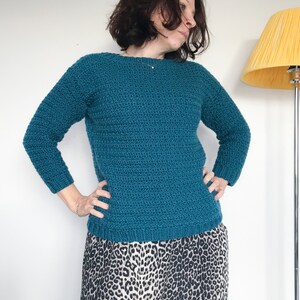 May include: A teal blue crocheted sweater with long sleeves. The sweater has a round neckline and a textured stitch pattern.