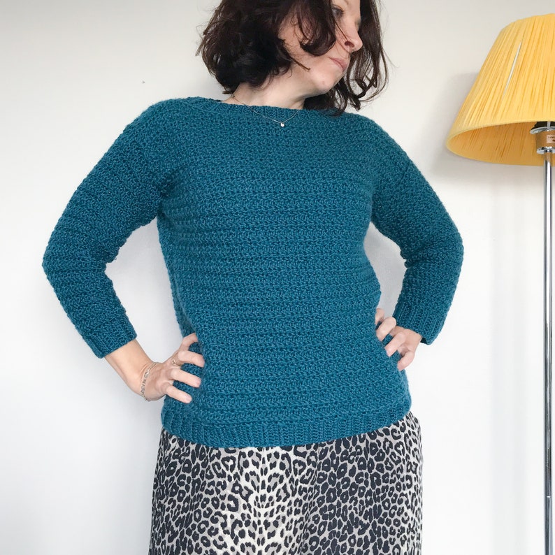 May include: A teal blue crocheted sweater with long sleeves. The sweater has a round neckline and a textured stitch pattern.