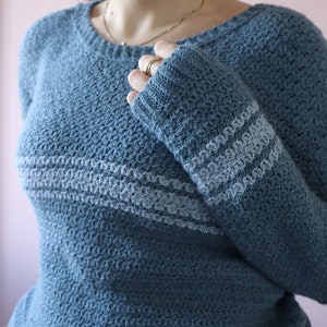 A close up of the ribbed cuff on a blue crochet sweater with lighter blue stripes.