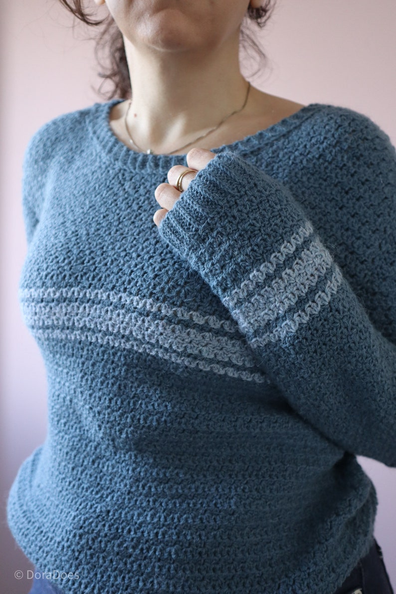 A close up of the ribbed cuff on a blue crochet sweater with lighter blue stripes.