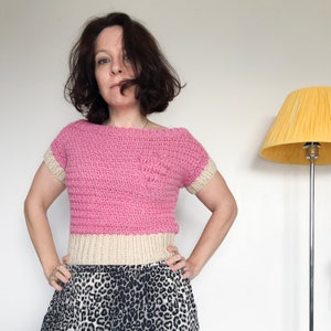 May include: A pink and cream crocheted top with short sleeves. The top is cropped and has a relaxed fit.