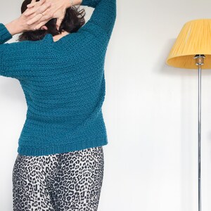 May include: A teal blue knitted sweater with long sleeves. The sweater is worn over a pair of black and white leopard print pants.