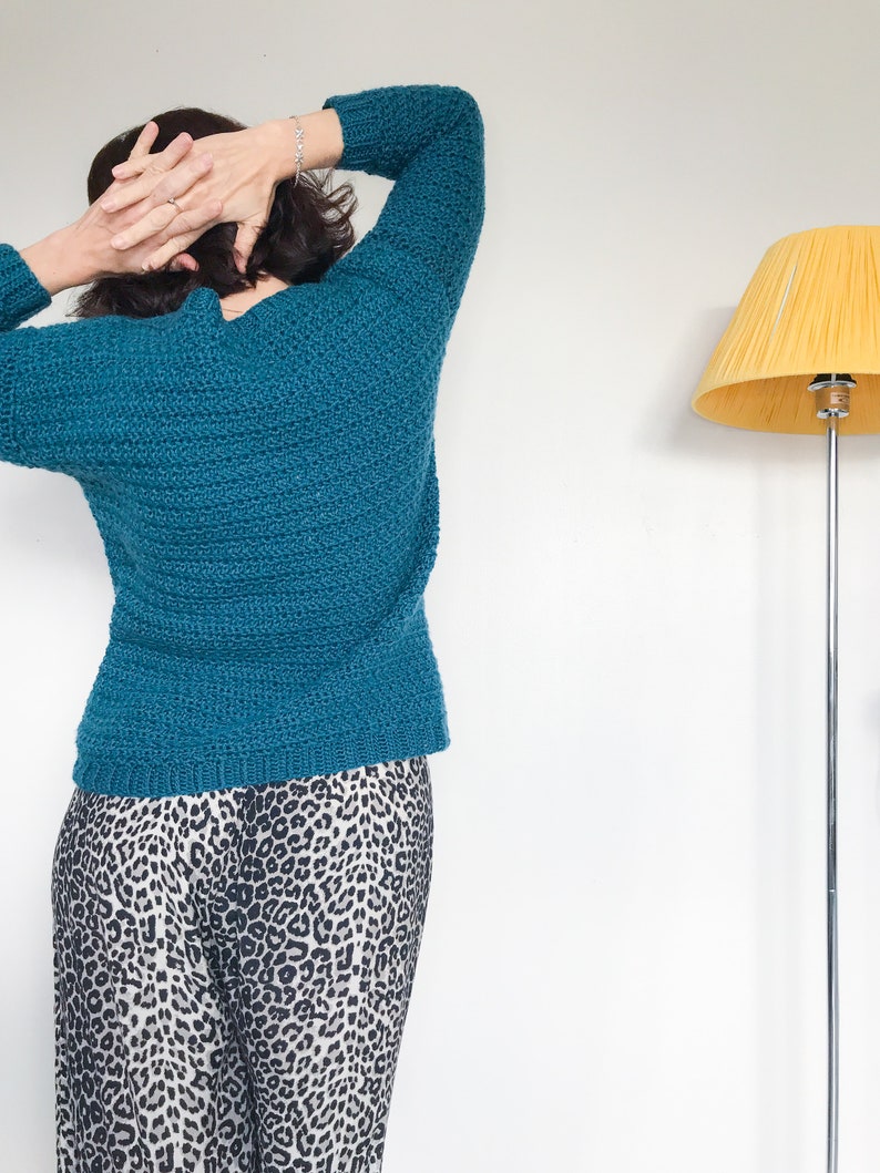 May include: A teal blue knitted sweater with long sleeves. The sweater is worn over a pair of black and white leopard print pants.