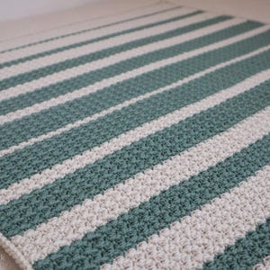 May include: A striped crocheted rug with alternating white and teal stripes. The rug is made with a textured stitch.