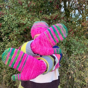 May include: A pair of pink and green striped knit mittens. The mittens are made of a soft, fuzzy yarn and have a colorful striped pattern.