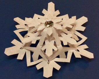May include: A white paper snowflake ornament with a sparkly finish and a clear rhinestone in the center.