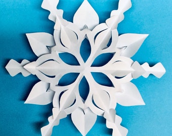 May include: A white paper snowflake with intricate cutouts, against a blue background.