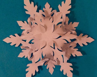 May include: A delicate, paper snowflake with intricate cutouts, crafted in a pale pink color. The snowflake is symmetrical and has a 3D effect, with its points folded and layered. It is displayed against a vibrant teal background.