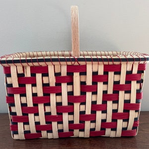 May include: A woven basket with a red and black checkered pattern and a wooden handle.