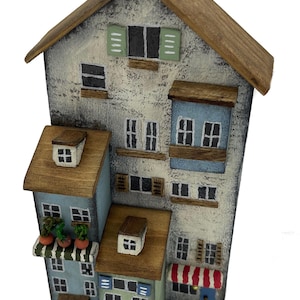 May include: A wooden model of a multi-story building with a blue, green, and white exterior. The building has a red and white striped awning and several windows. The model is painted in a rustic style.
