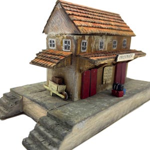 May include: A wooden model of a train station with a red roof and red doors. The station is labeled "INVERNADA".