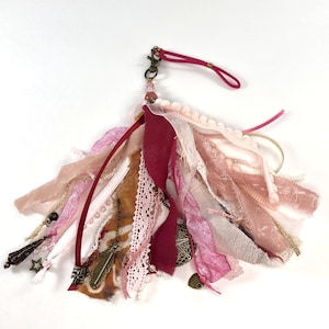 May include: A pink and burgundy fabric tassel keychain with a metal clasp and various charms, including feathers, stars, and hearts.