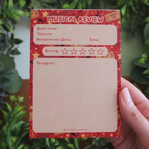May include: A red and cream-coloured musical review notepad with a musical note and star pattern. The notepad includes sections for show details, a rating system, and space for thoughts. The text "MUSICAL REVIEW" is at the top.