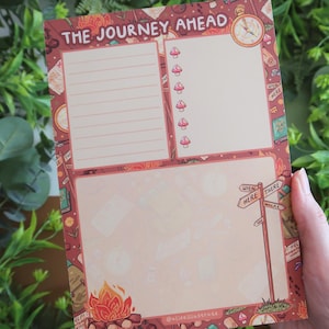 May include: A notepad with a burgundy border and the text "THE JOURNEY AHEAD". The notepad features sections for notes, a compass, mushrooms, a campfire, and a signpost with "WHEN HERE THERE WHERE".